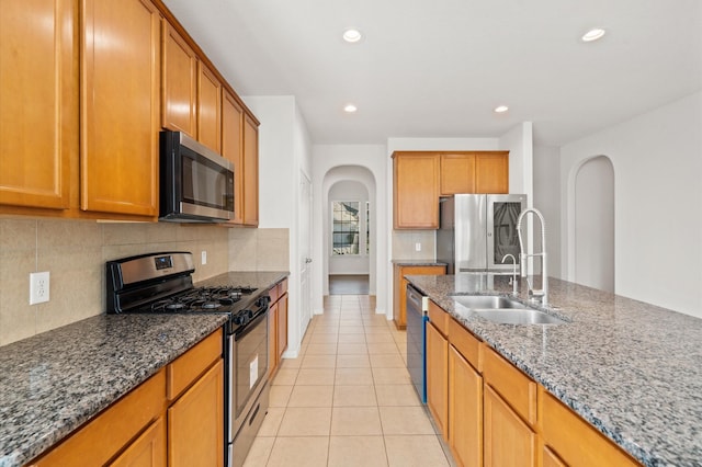 kitchen with stainless steel appliances, sink, stone countertops, backsplash, and light tile patterned flooring