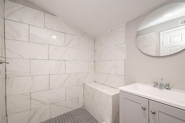 bathroom with tiled shower, vanity, and lofted ceiling