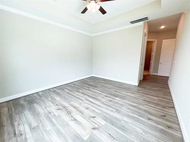 spare room with ceiling fan, light hardwood / wood-style floors, a tray ceiling, and ornamental molding