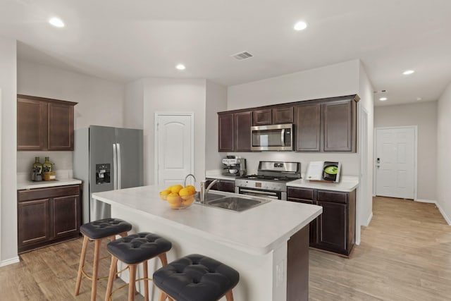 kitchen featuring appliances with stainless steel finishes, sink, light wood-type flooring, a breakfast bar, and a center island with sink