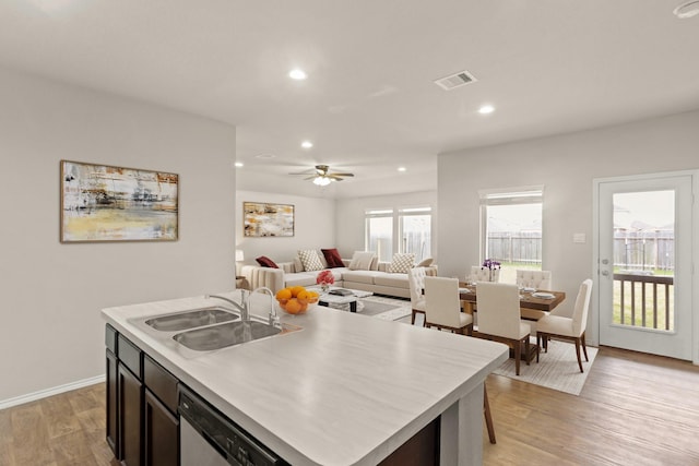 kitchen featuring sink, light wood-type flooring, ceiling fan, stainless steel dishwasher, and a center island with sink