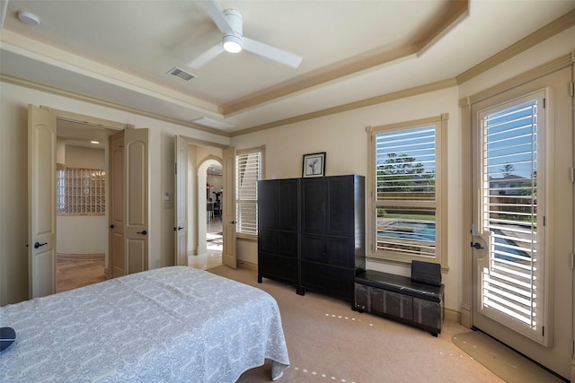 bedroom with a tray ceiling, light colored carpet, visible vents, ornamental molding, and a ceiling fan