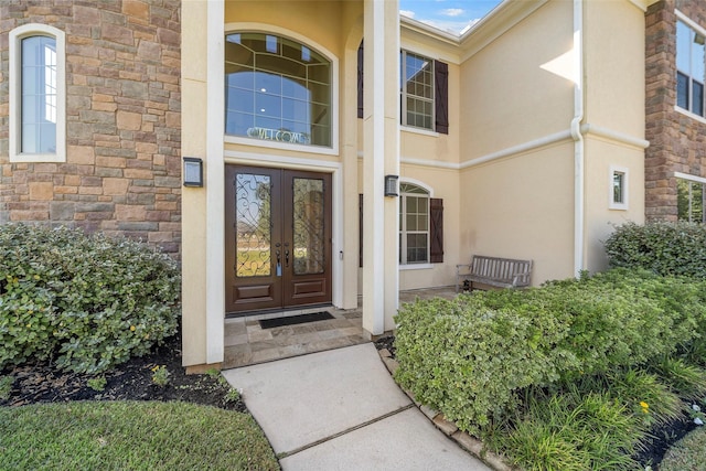 property entrance featuring stone siding, french doors, and stucco siding