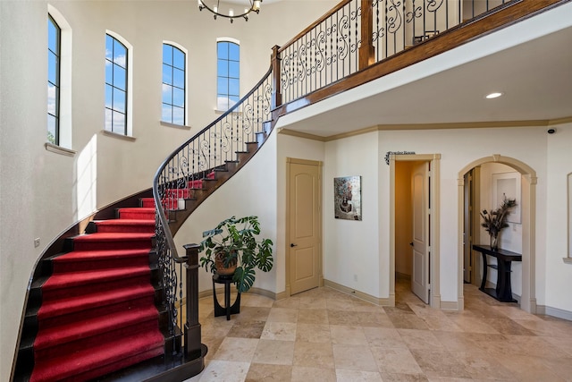 staircase with arched walkways, recessed lighting, a towering ceiling, baseboards, and crown molding