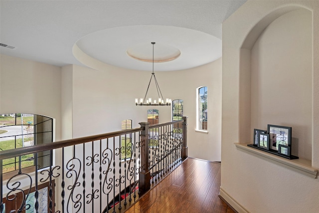 hallway with a chandelier, plenty of natural light, wood finished floors, and visible vents