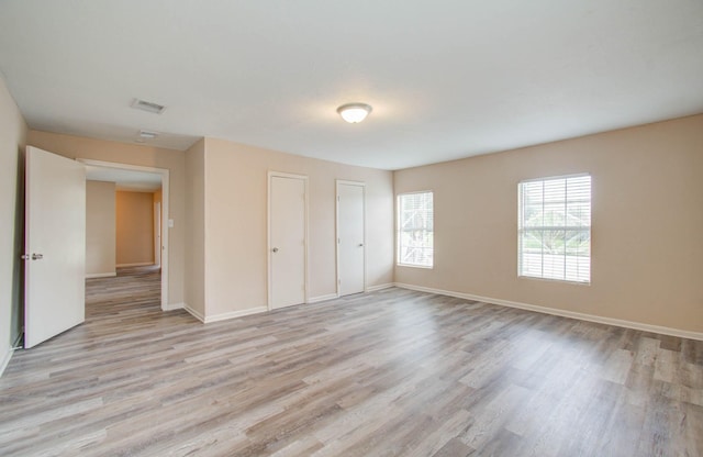 unfurnished bedroom featuring light wood-type flooring and multiple closets