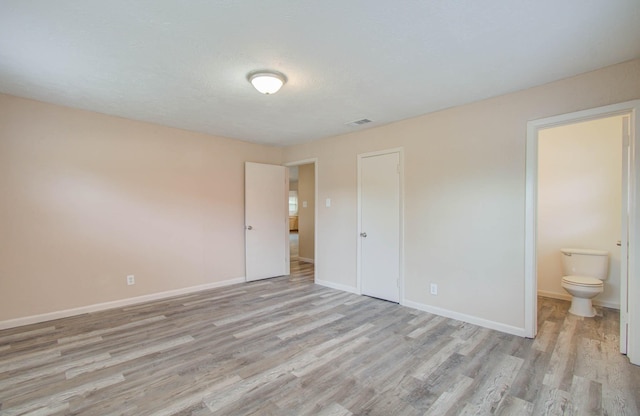 unfurnished bedroom with light hardwood / wood-style floors, a closet, and ensuite bath