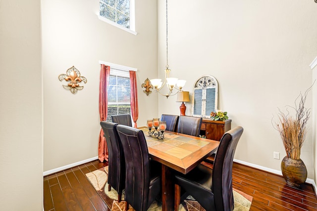 dining area with dark hardwood / wood-style floors, a towering ceiling, and an inviting chandelier