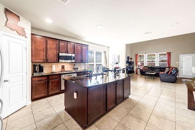 kitchen featuring stainless steel appliances, sink, backsplash, a kitchen island with sink, and light tile patterned floors