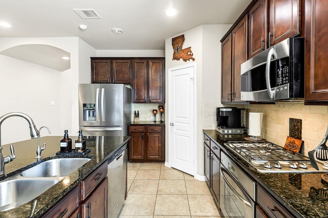 kitchen with sink, backsplash, dark stone counters, light tile patterned flooring, and stainless steel appliances