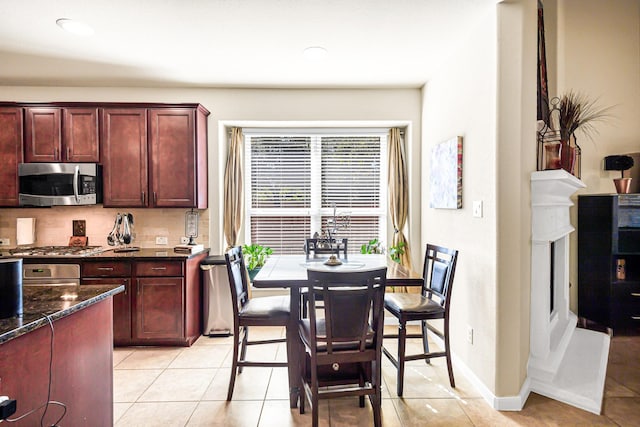 kitchen featuring light tile patterned flooring, backsplash, dark stone counters, and appliances with stainless steel finishes