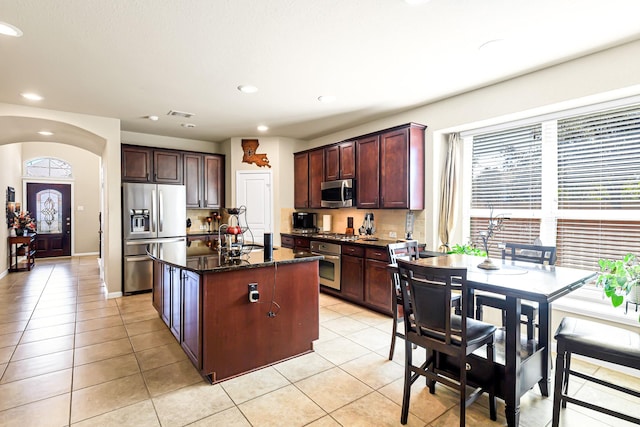 kitchen with light tile patterned floors, stainless steel appliances, dark stone counters, and a kitchen island