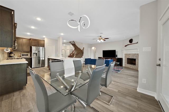 dining area featuring sink, a tiled fireplace, light hardwood / wood-style flooring, and ceiling fan