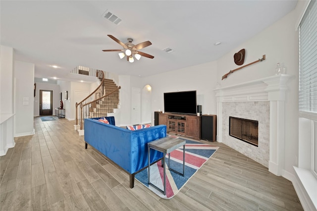 living room with light wood-type flooring, ceiling fan, and a tiled fireplace