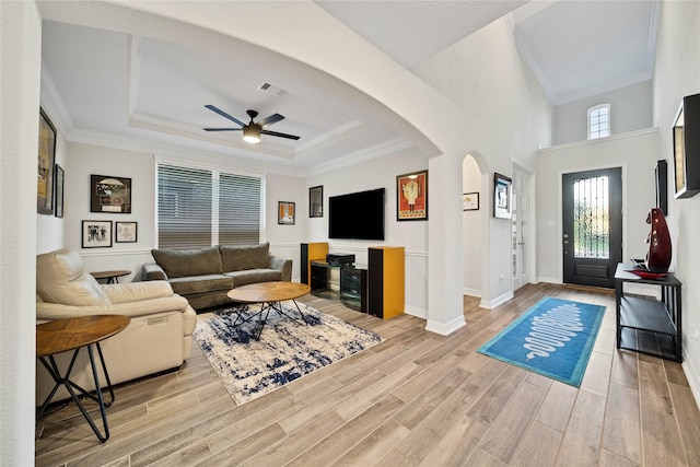 living room featuring crown molding, light hardwood / wood-style floors, ceiling fan, and a tray ceiling