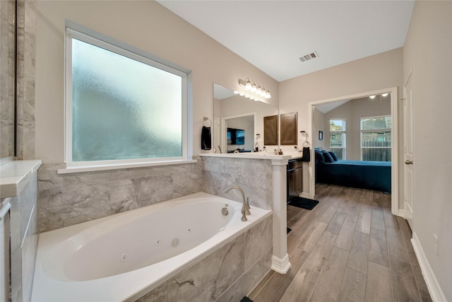 bathroom featuring vanity, hardwood / wood-style flooring, tiled tub, and lofted ceiling