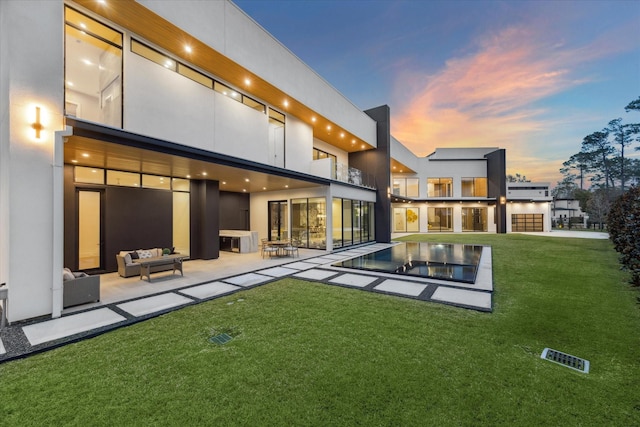 back house at dusk with an outdoor living space, a patio, and a yard