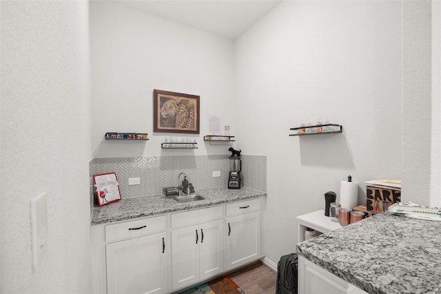 bar with sink, tasteful backsplash, light stone counters, wood-type flooring, and white cabinets