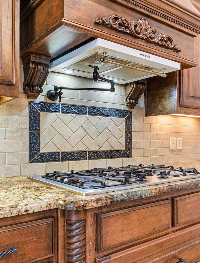 kitchen featuring light stone countertops, premium range hood, stainless steel gas cooktop, and tasteful backsplash