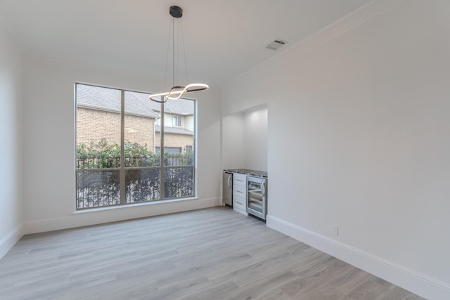 unfurnished dining area with crown molding, beverage cooler, and light wood-type flooring