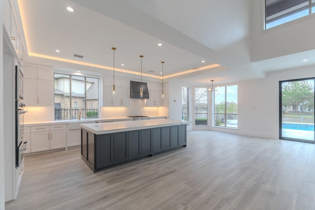 kitchen with decorative light fixtures, white cabinetry, a center island, a tray ceiling, and wall chimney exhaust hood