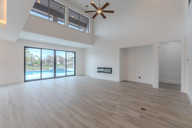 unfurnished living room featuring a high ceiling, ceiling fan, and light hardwood / wood-style floors