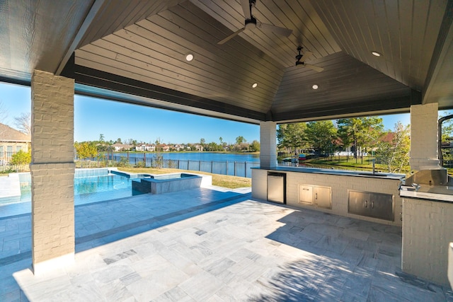 view of pool with a gazebo, a water view, ceiling fan, exterior kitchen, and a patio