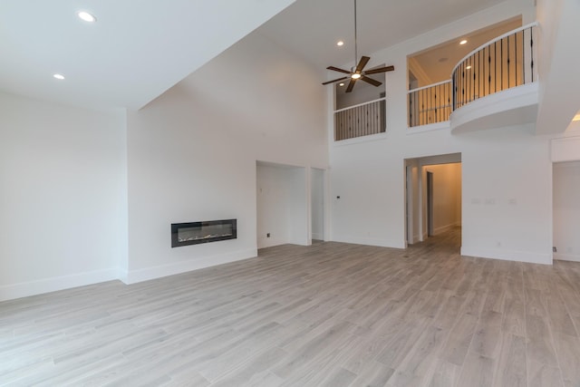 unfurnished living room with ceiling fan, a towering ceiling, and light hardwood / wood-style floors