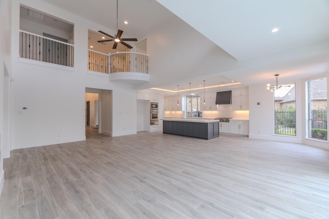 unfurnished living room featuring a towering ceiling, ceiling fan with notable chandelier, and light hardwood / wood-style flooring