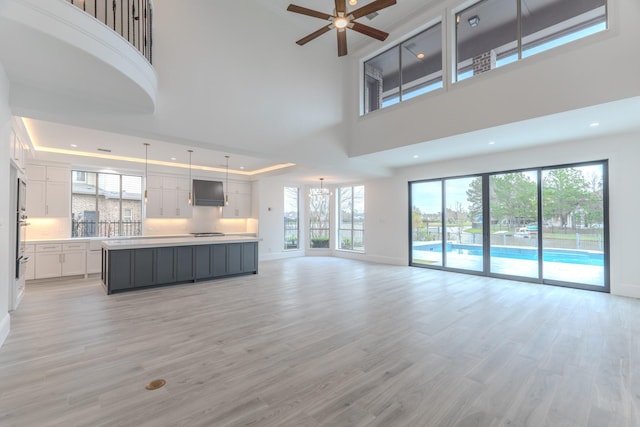 unfurnished living room featuring ceiling fan, a raised ceiling, light hardwood / wood-style flooring, and a high ceiling