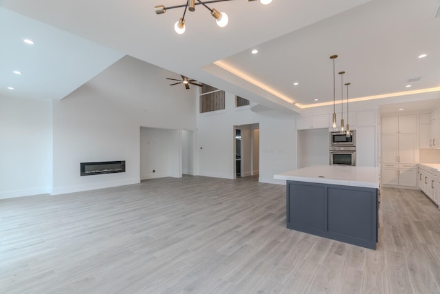 kitchen with hanging light fixtures, appliances with stainless steel finishes, a raised ceiling, a kitchen island, and white cabinets