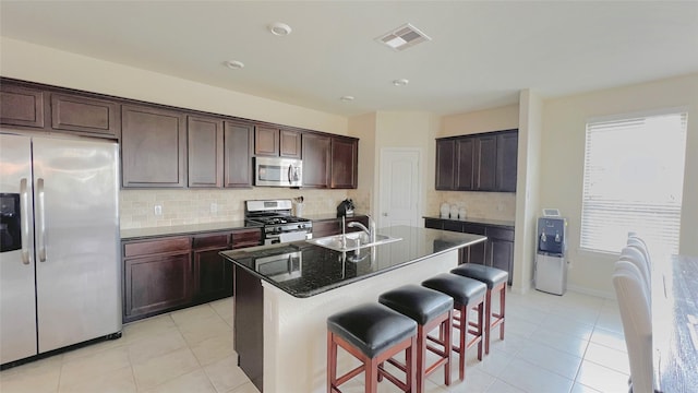 kitchen with stainless steel appliances, tasteful backsplash, dark stone countertops, sink, and a kitchen island with sink