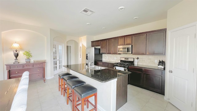 kitchen featuring appliances with stainless steel finishes, a kitchen bar, dark stone counters, tasteful backsplash, and a kitchen island with sink