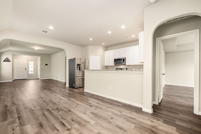 kitchen featuring appliances with stainless steel finishes, backsplash, hardwood / wood-style flooring, white cabinetry, and light stone countertops