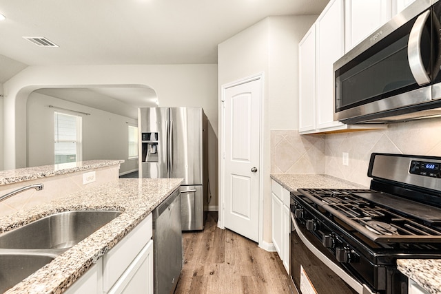 kitchen with appliances with stainless steel finishes, sink, white cabinets, light wood-type flooring, and light stone counters