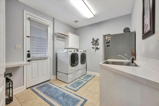 laundry room with a textured ceiling, light tile patterned floors, sink, separate washer and dryer, and cabinets