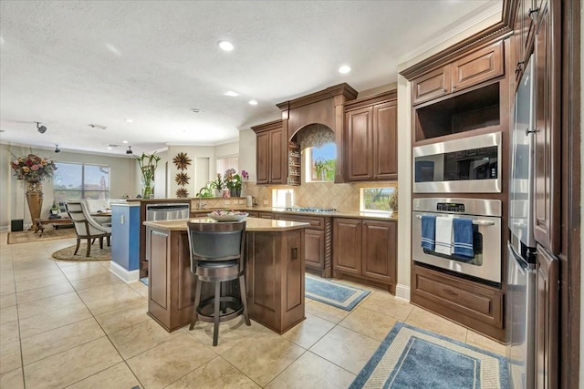 kitchen with kitchen peninsula, appliances with stainless steel finishes, backsplash, a kitchen bar, and a center island