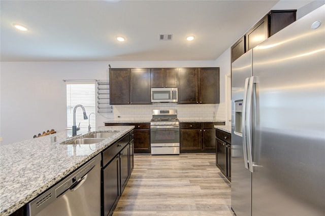 kitchen with sink, tasteful backsplash, dark brown cabinets, light hardwood / wood-style flooring, and stainless steel appliances