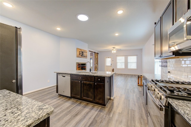 kitchen featuring sink, stainless steel appliances, light stone countertops, and a center island with sink