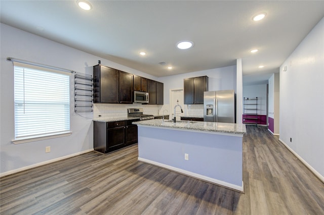 kitchen with backsplash, dark brown cabinets, stainless steel appliances, dark hardwood / wood-style floors, and an island with sink