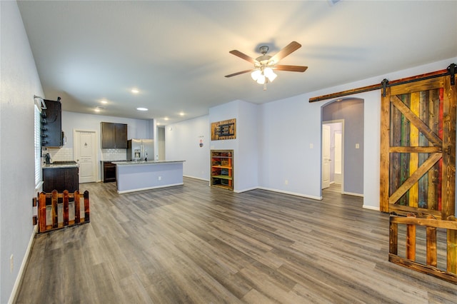 living room with a barn door, dark wood-type flooring, and ceiling fan