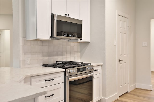 kitchen featuring backsplash, stainless steel appliances, light stone counters, light hardwood / wood-style floors, and white cabinets