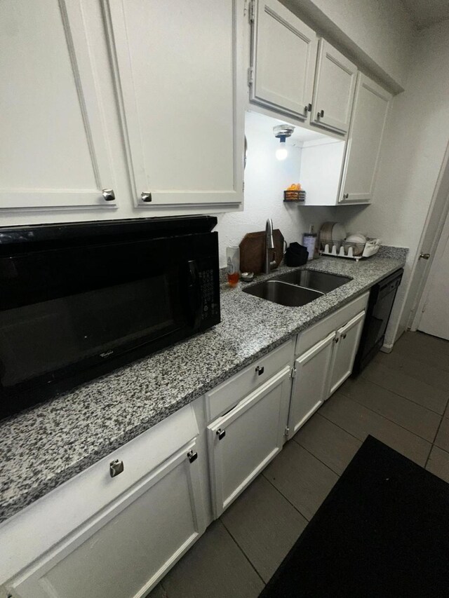 kitchen with sink, white cabinets, light stone counters, dark tile patterned flooring, and black appliances