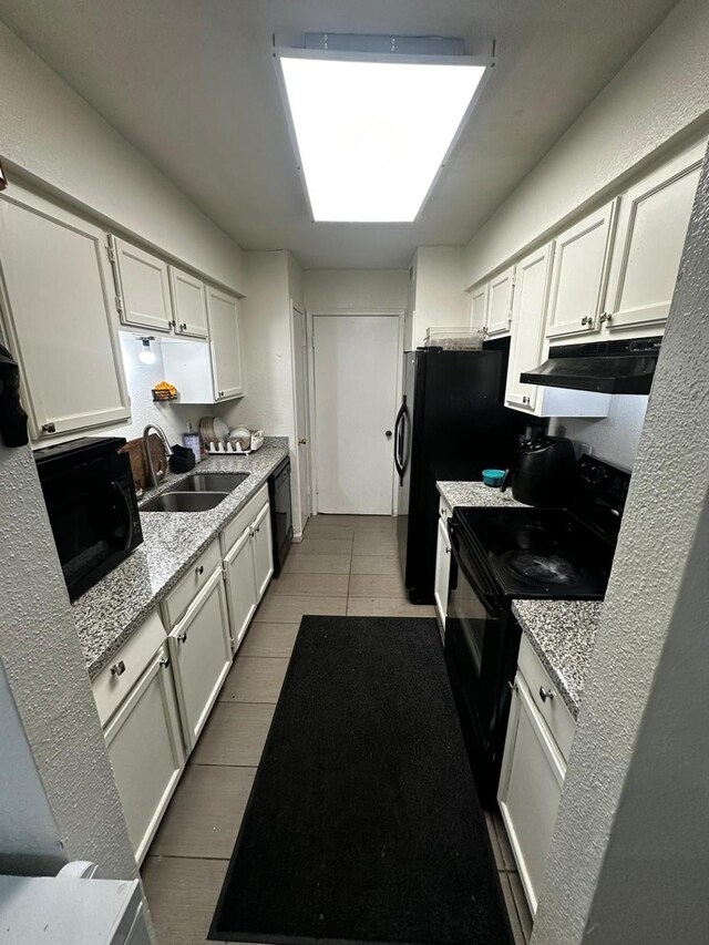 kitchen featuring black appliances, light stone countertops, white cabinets, sink, and tile patterned floors