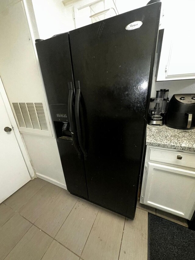 kitchen with white cabinetry, light stone counters, light tile patterned floors, and black fridge