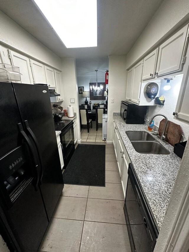 kitchen with sink, white cabinetry, light tile patterned floors, light stone counters, and black appliances