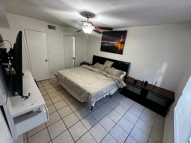 bedroom featuring ceiling fan, light tile patterned floors, and a textured ceiling