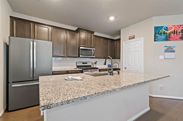 kitchen with light stone countertops, stainless steel appliances, sink, a kitchen island with sink, and dark brown cabinets