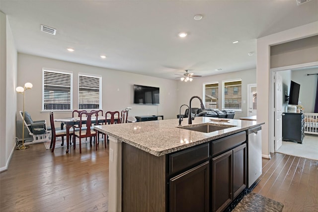 kitchen with dark brown cabinets, stainless steel dishwasher, sink, hardwood / wood-style floors, and a kitchen island with sink