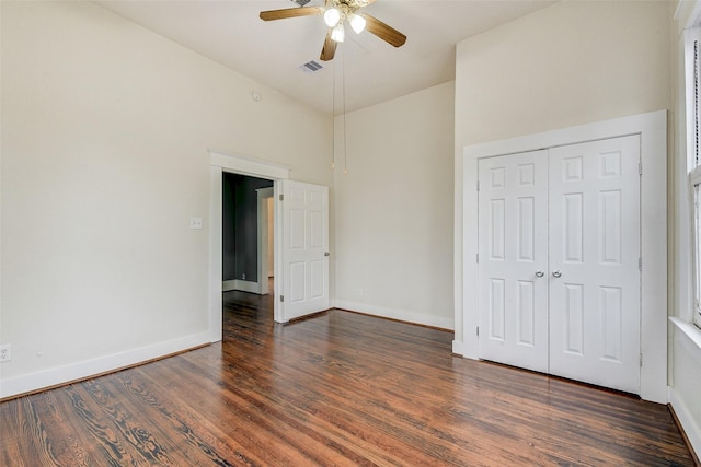 unfurnished bedroom with a closet, a high ceiling, ceiling fan, and dark hardwood / wood-style flooring